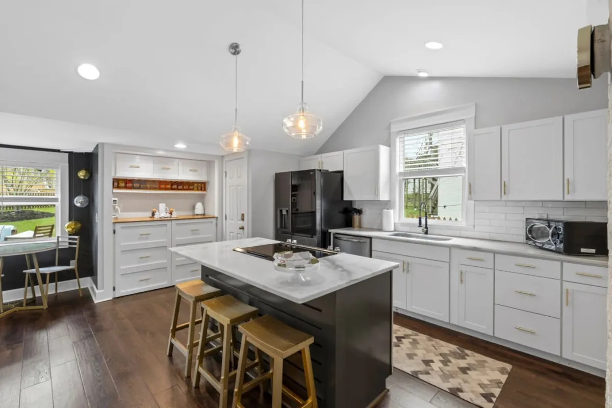 A contemporary, open kitchen space with a central island featuring bar seating. Modern stainless appliances line the walls, while large windows bathe the area in natural light. The island is set up for casual meals or entertaining, and the atmosphere feels lively and inviting.