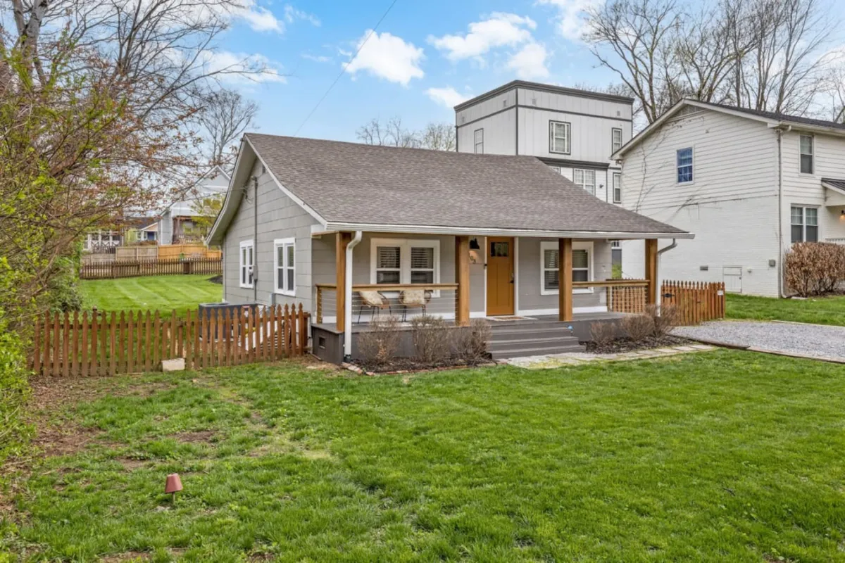 This image features the welcoming front porch of the home, complete with comfortable seating, a green lawn, and a fenced yard in the background. The setup invites residents to enjoy morning coffee or watch children play in the yard. The porch is framed by thoughtful landscaping and the privacy fence ensures a sense of seclusion.