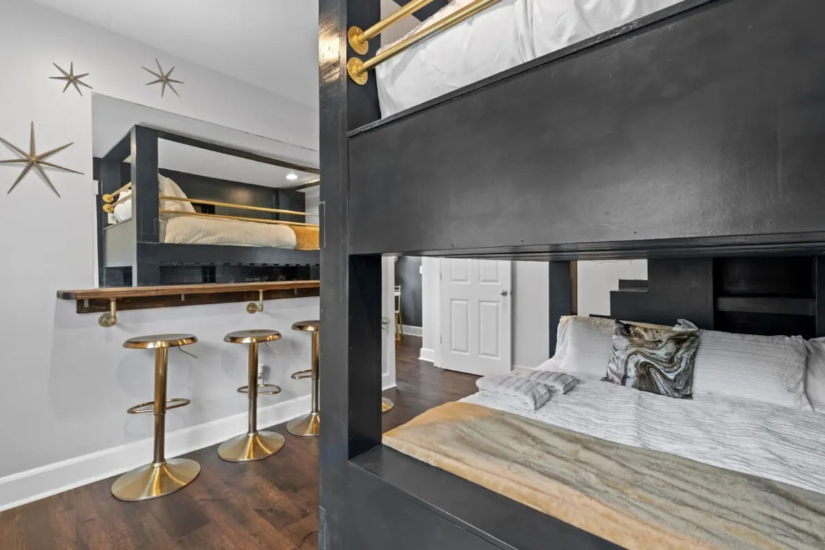This image showcases a playful bedroom featuring queen-over-queen bunk beds, golden bar stools, and whimsical decorative wall stars, creating a vibrant and welcoming space for kids or families to gather.
