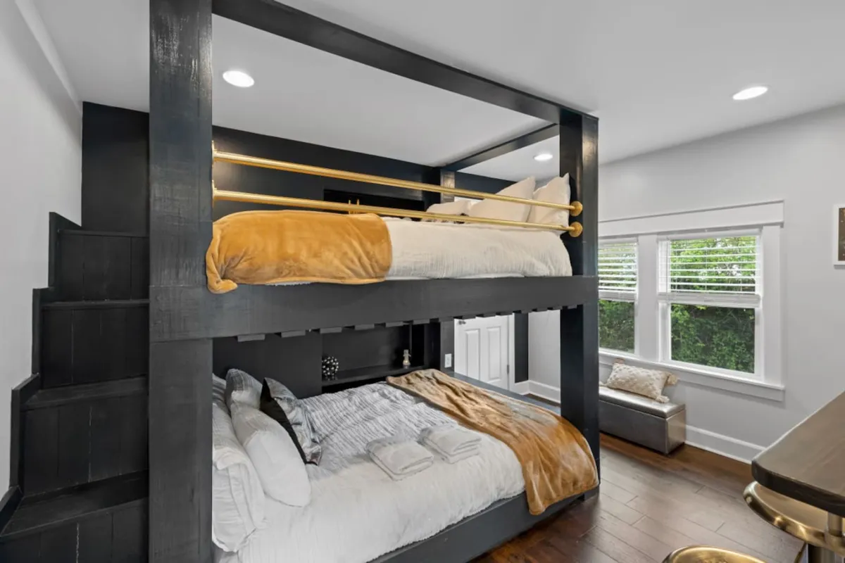A cheerful, inviting bedroom with queen-over-queen bunk beds, playful decorative throw pillows, and a cozy window seat. The space feels perfect for families or groups, offering both comfort and a sense of whimsy.