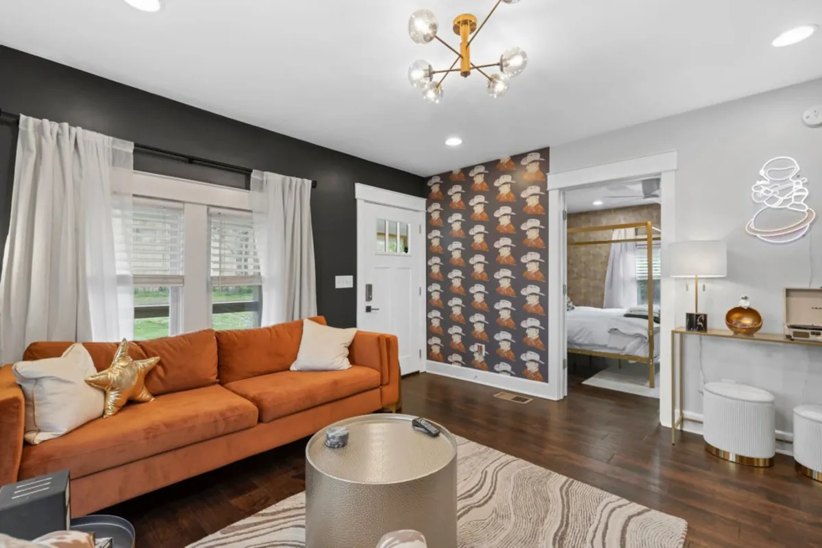 A stylish living room with a vibrant orange sofa, decorative wallpaper, and a chic gold table. The space feels cozy yet lively, ideal for relaxing, movie nights, or socializing with loved ones.