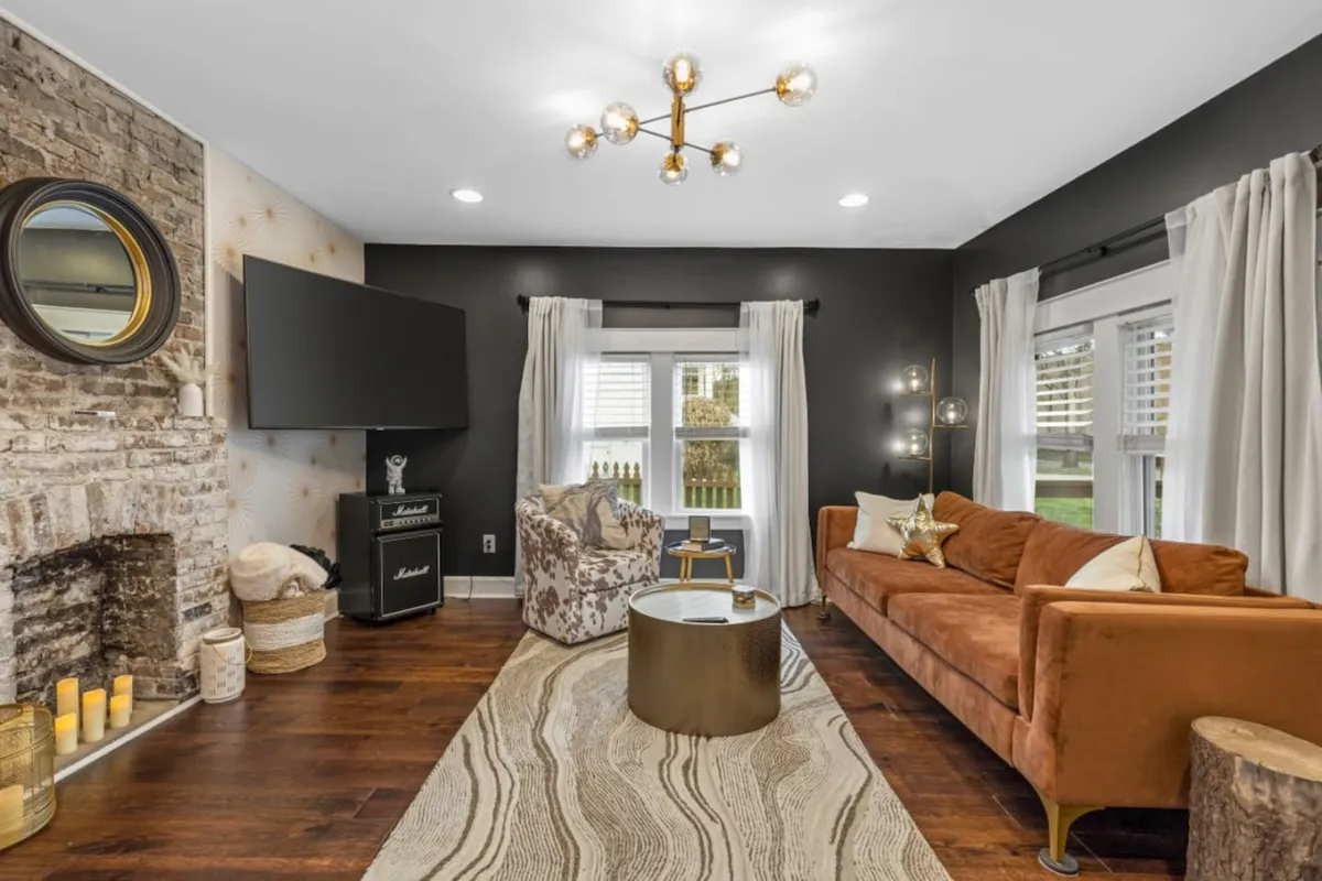 The image shows a stylish, comfortable living room with a plush sofa, inviting armchair, chic coffee table, large TV, and a cozy fireplace, all arranged to create a welcoming space for guests to relax and gather.