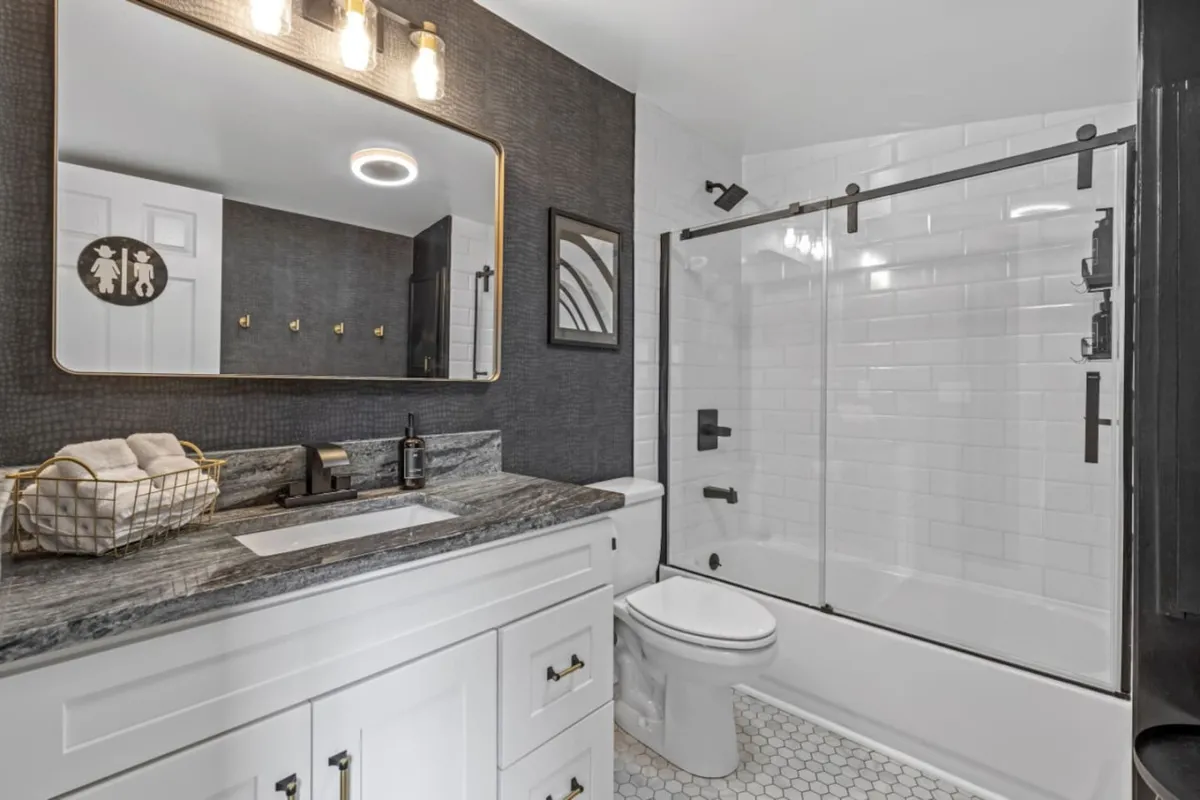 A contemporary bathroom with a modern sink and vanity, a framed mirror, and a glass-door shower set against stylish hexagonal floor tiles. The space is bright and fresh, ideal for daily routines and self-care.